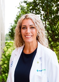 Dr. Tenkman, female appearance in a white lab coat with long curly hair.
