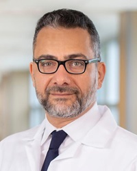 Head shot of a man in a white shirt, black tie, wearing a doctor's white labcoat
