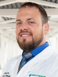 man with short hair and a beard wearing a blue shirt and a white doctor's coat