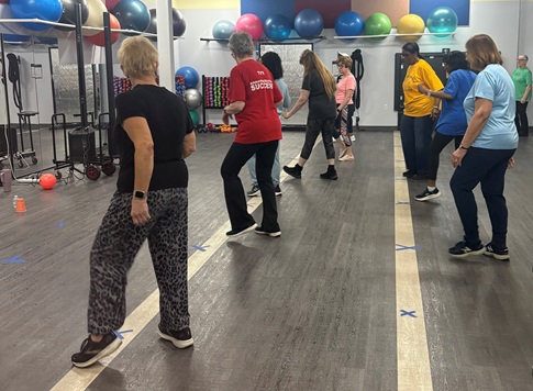 Dance fitness class at St. Joes At The Mall. Image of about a dozen people dressed in fitness clothes arranged in lines in dance studio.