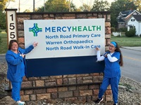 members of North Rd. Walk in Care staff wearing blue scrubs standing in front of building sign.